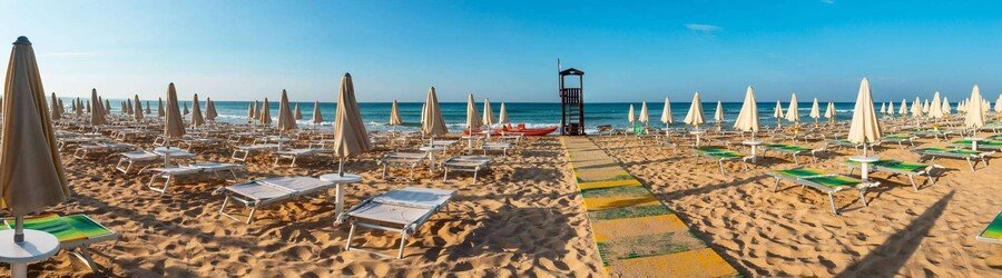 Sandy beach with rows of umbrellas and calm shallow water in Pescoluse Puglia