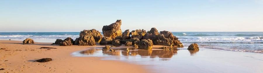 Rocky shoreline and calm waves on a golden sandy beach in Victoria, Australia.