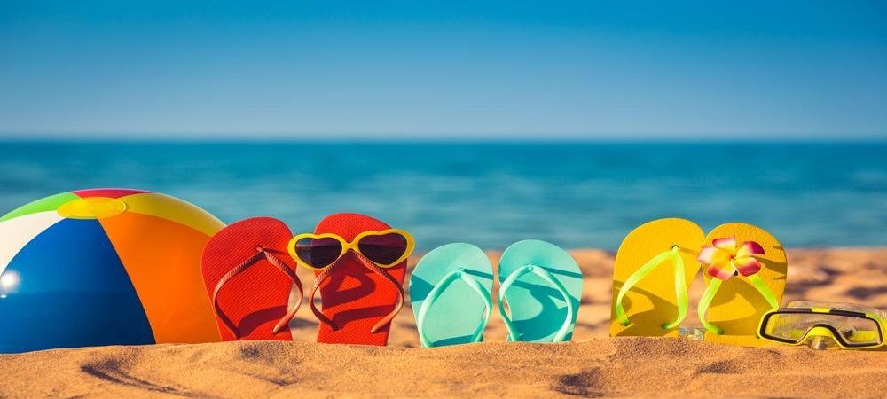 Best beach gear essentials — sandals, snorkel, fins, and a bright beach ball on the sand by the sea.