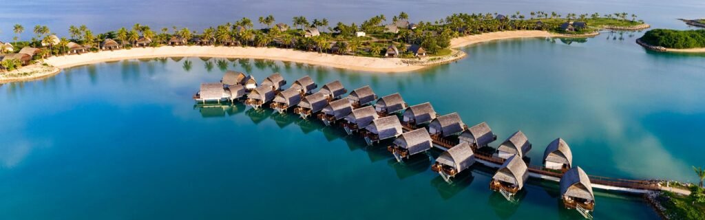 Aerial view of the overwater bures at Fiji Marriott Resort Momi Bay above a calm blue lagoon.