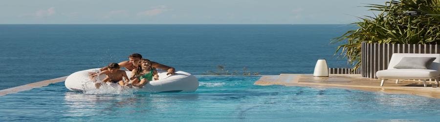 Family enjoying a large inflatable pool float with an ocean view in the background.