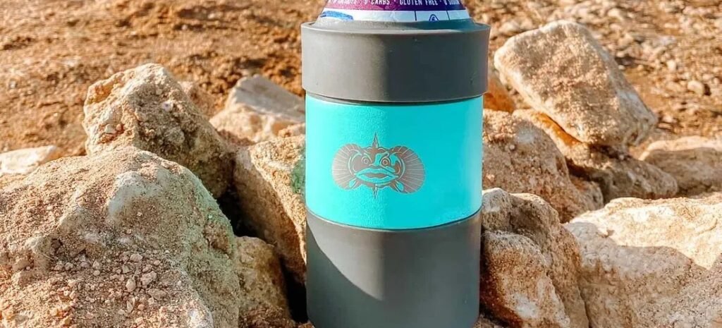 Colorful beach drink accessories including koozies and can coolers displayed by the ocean on a sunny day.