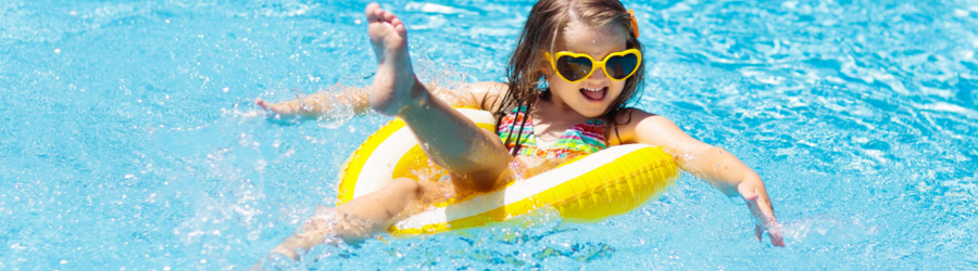 Happy little girl splashing in the pool on a yellow inflatable ring with heart-shaped sunglasses.