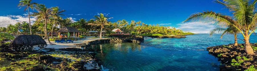 Coastal resort area in American Samoa with palm trees, beach huts, and clear turquoise water.