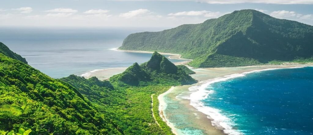 Aerial view of lush green cliffs and turquoise reefs along the coast of American Samoa. The stunning beaches of American Samoa