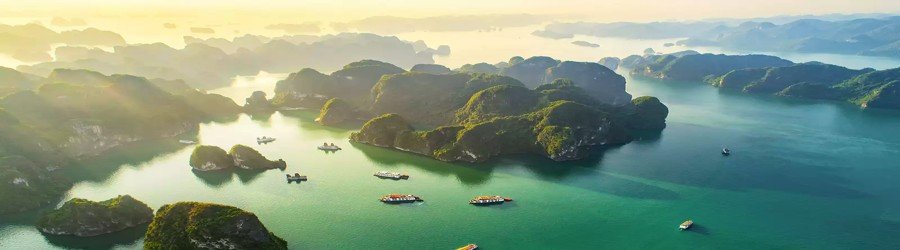 Morning sunlight over Halong Bay highlighting limestone islets and calm turquoise waters.