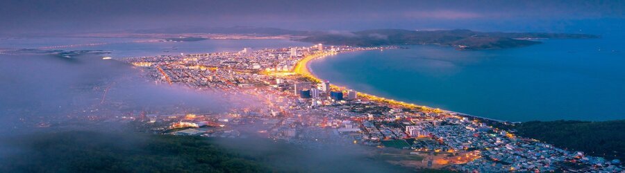 Aerial view of Binh Dinh’s coastline illuminated at dusk, curving along the vibrant city.