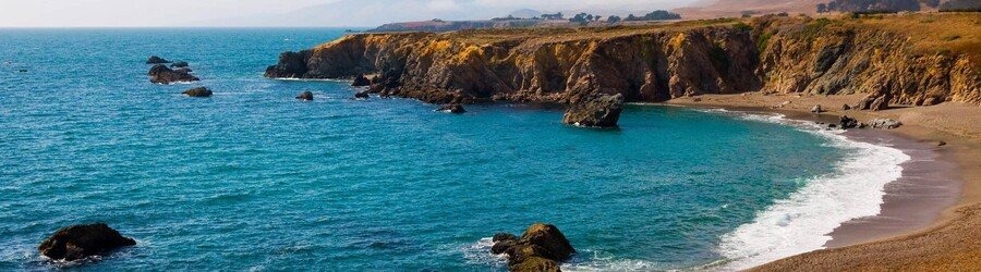 Rocky coastline and bright blue water along a wide, scenic beach on California’s North Coast.