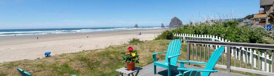 Oceanfront deck with turquoise chairs overlooking Cannon Beach and Haystack Rock.