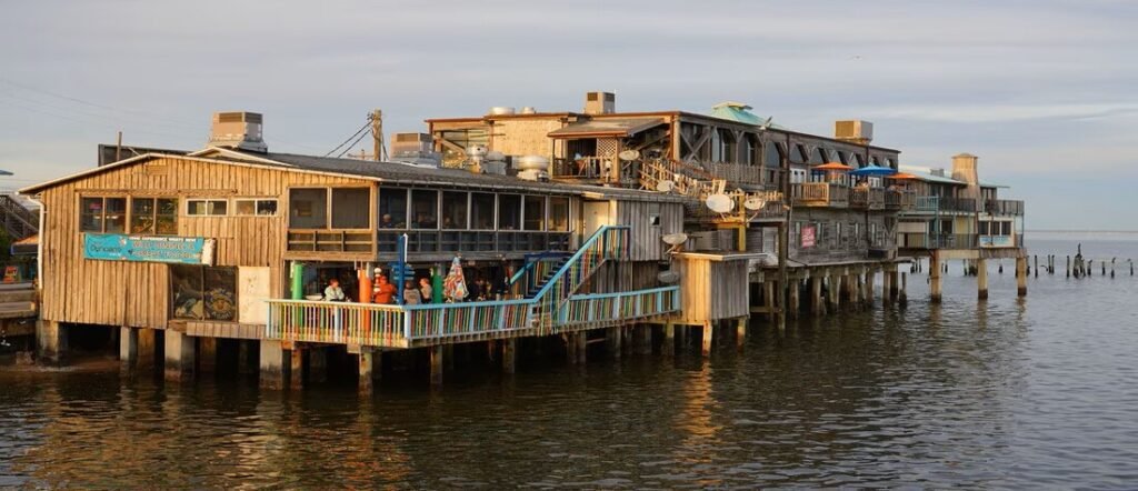 Rustic waterfront restaurant on stilts in Cedar Key Florida, overlooking calm Gulf waters at sunset.