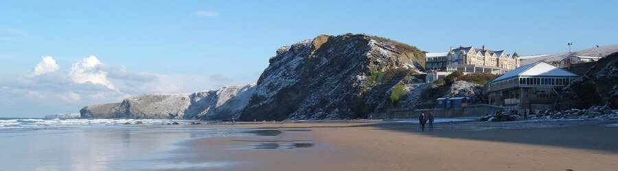 Dramatic seaside cliffs and a beachfront hotel overlooking the wide sandy beach in Cornwall UK.