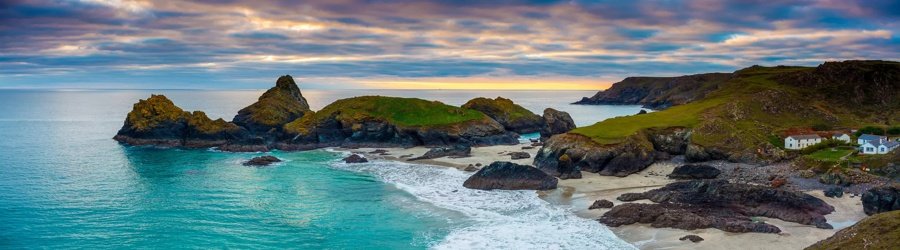 Kynance Cove’s rocky cliffs and turquoise sea under a colorful sunset on the Cornwall coast, UK.