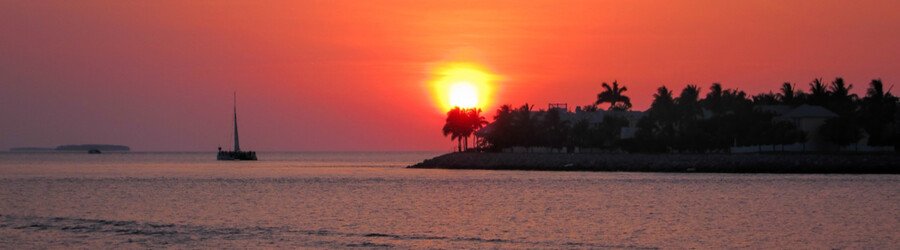 Sunset over the calm waters of the Florida Keys with a sailboat on the horizon.