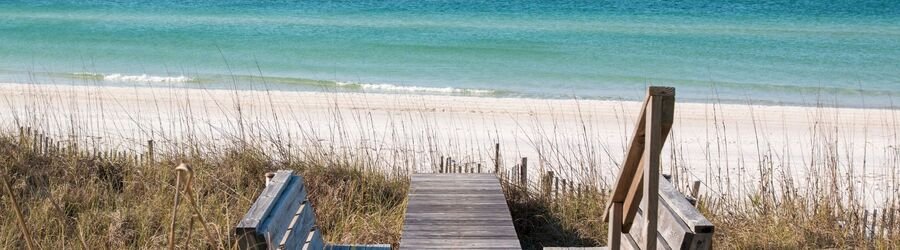 wooden boardwalk leading to grayton beach florida with white sand and emerald gulf water