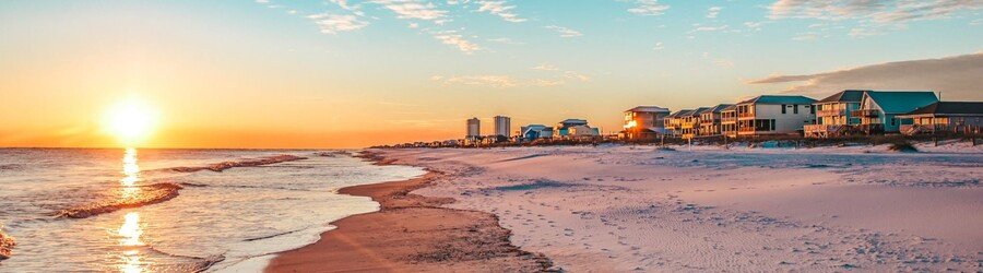 Sunrise over Gulf Shores Alabama with beach houses along the coast and glowing orange light on the sand.