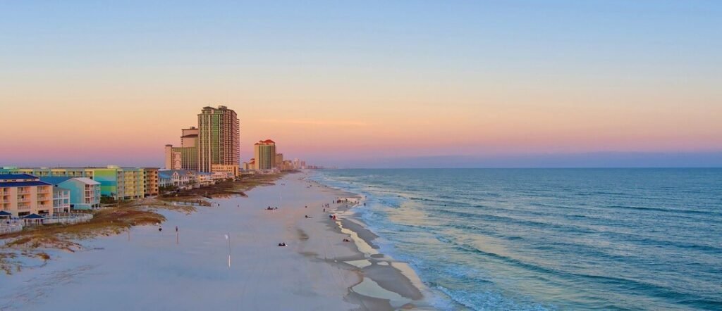 Gulf Shores Alabama beach at sunrise with calm waves, soft white sand, and pastel colors along the shoreline.