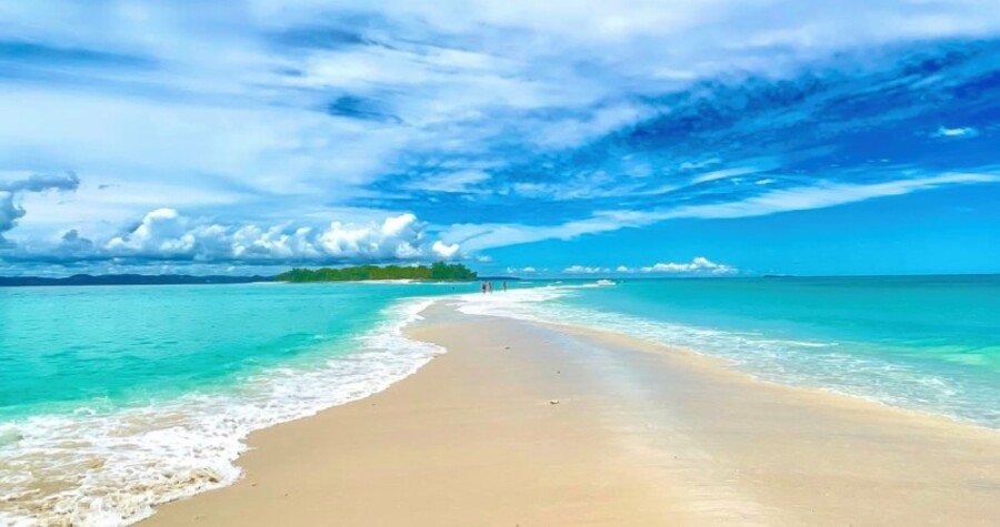 A bright turquoise lagoon and long white-sandbar stretch across Nosy Iranja Madagascar under a vivid blue sky.