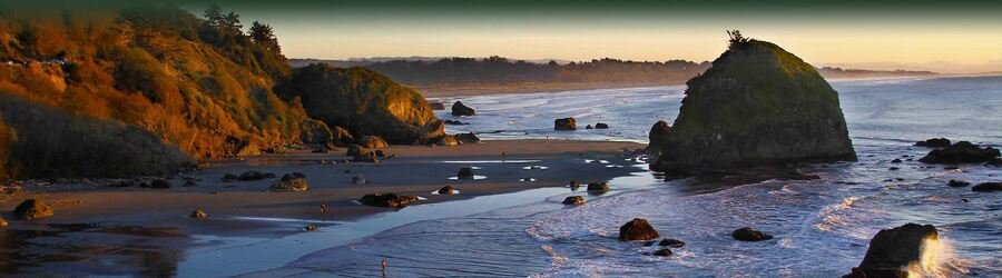 Sunset light over a wide sandy beach with sea stacks, rocky outcrops, and gentle waves along the Humboldt County coastline.