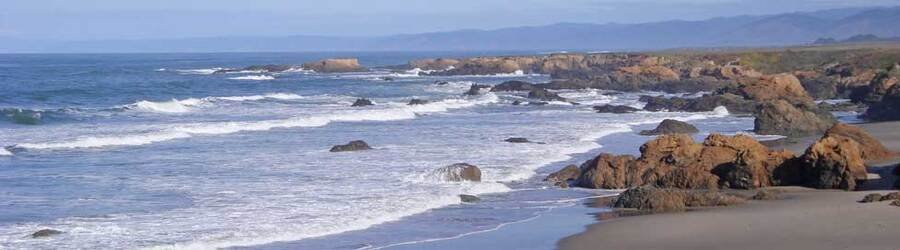 A rugged Northern California beach with rock formations scattered along the sand and waves breaking at the shoreline.