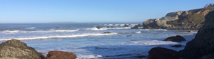 Rocky Marin County coastline with waves breaking against large boulders beneath coastal cliffs.