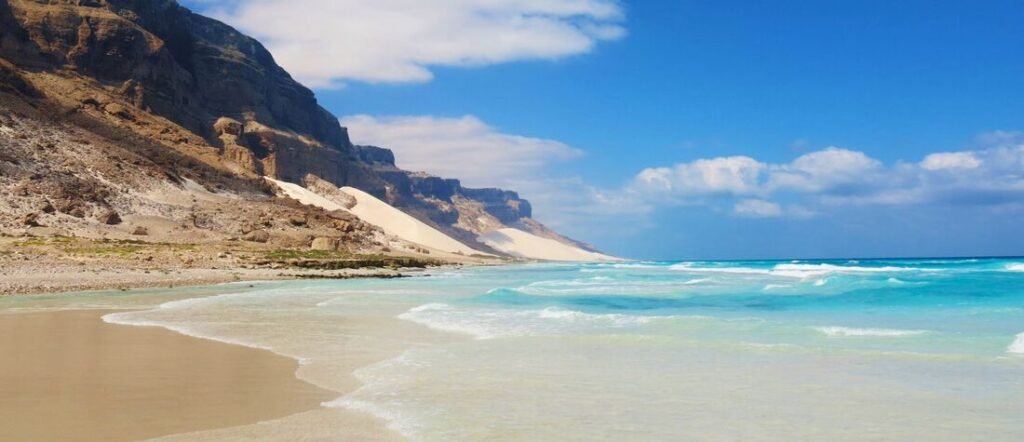 Turquoise waves and sweeping white sand dunes along the coastline of Socotra Island, Yemen.