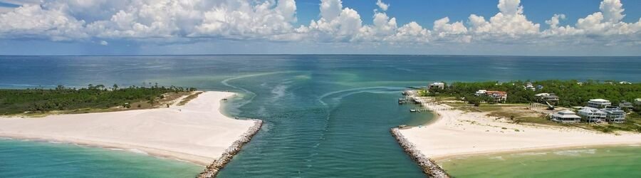 Aerial view of St. George Island Florida showing turquoise water dividing two pristine white-sand shores under bright blue skies.