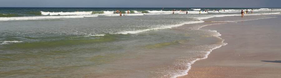 Visitors enjoying gentle waves along the sandy shoreline of St. George Island Florida on a warm sunny afternoon.