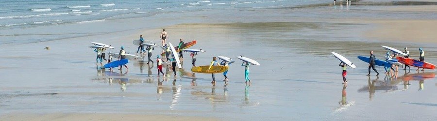 Surfers carrying boards along the golden sands of Newquay Beach on the Cornwall coast, UK.