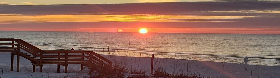 Sunset over the Gulf Shores beach with pink clouds and calm ocean waves.