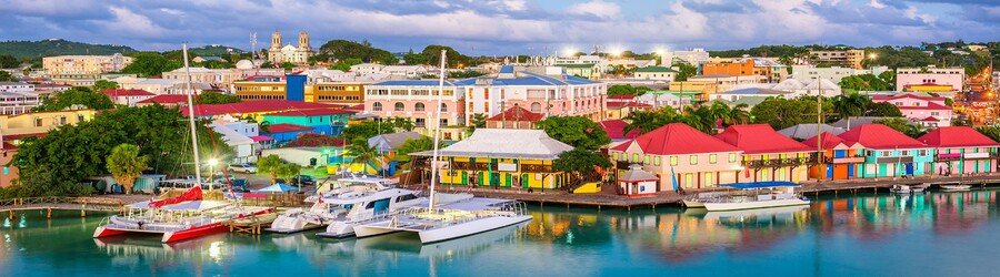 Colorful waterfront buildings in St. John’s, Antigua with boats docked along the calm harbor.