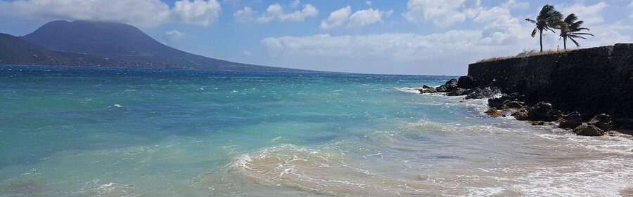 Cockleshell Beach in St. Kitts with turquoise waves, rocky shoreline, and Nevis visible in the distance.