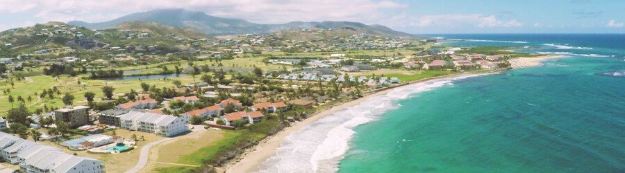 Aerial view of Frigate Bay Beach in St. Kitts with turquoise water, white sand, and hillside resorts.
