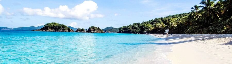White sand and bright turquoise water at Lindbergh Bay in St. Thomas, with palm trees and small islands in the distance.