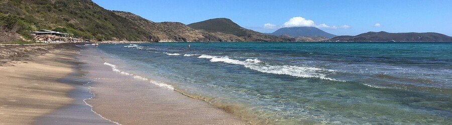 Shipwreck Beach in St. Kitts with calm waves, clear water, and views of Nevis in the distance.