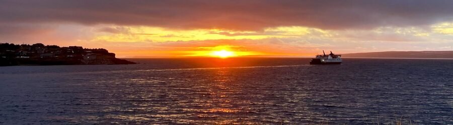 Ferry boat sailing across the water at sunrise near St. John’s with golden clouds and calm ocean reflections
