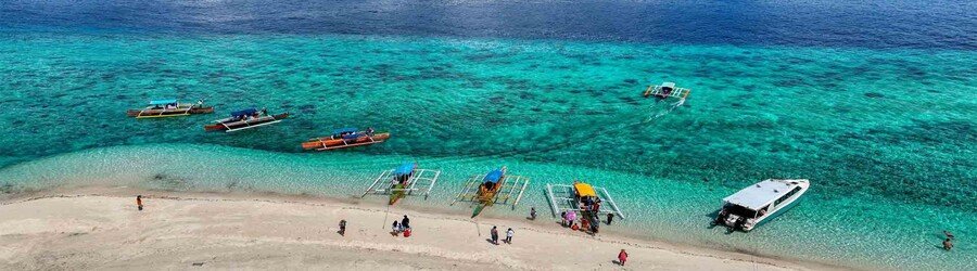 Boats anchored along a sandy beach in Camiguin Island with clear turquoise water