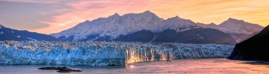 Alaska glacier glowing at sunset with snow-covered mountains in the background.