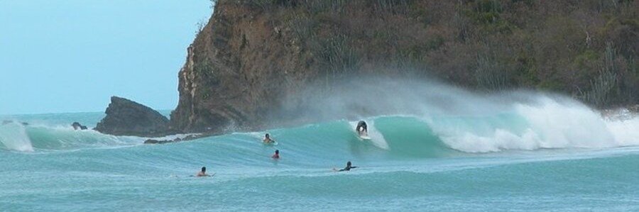 Surfers riding large breaking waves at Josiah’s Bay in Tortola