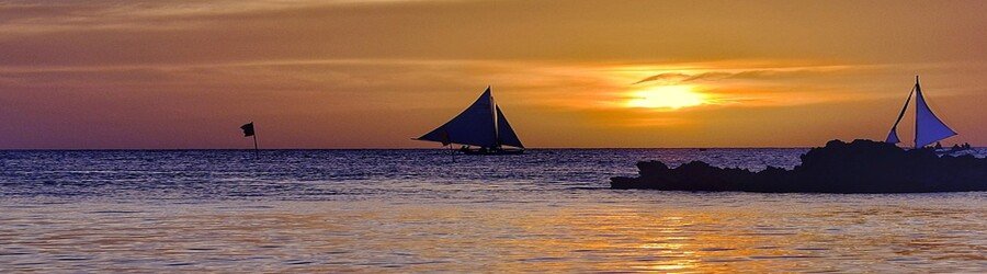Sunset over the sea on Samal Island with traditional boats silhouetted against the sky