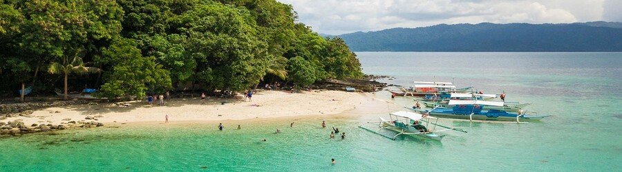 Small beach near San Vicente Palawan with clear water, outrigger boats, and forested shoreline