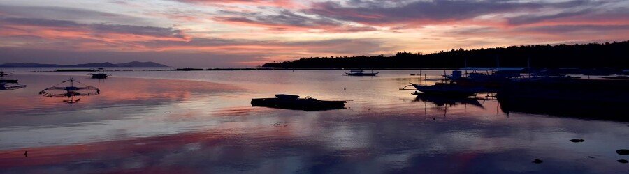 Sunset over calm water in San Vicente Palawan with small boats reflected on the surface