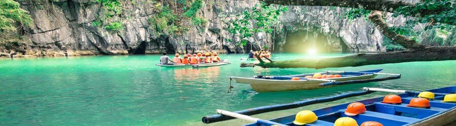 Small boats entering a limestone cave with emerald water near San Vicente Palawan