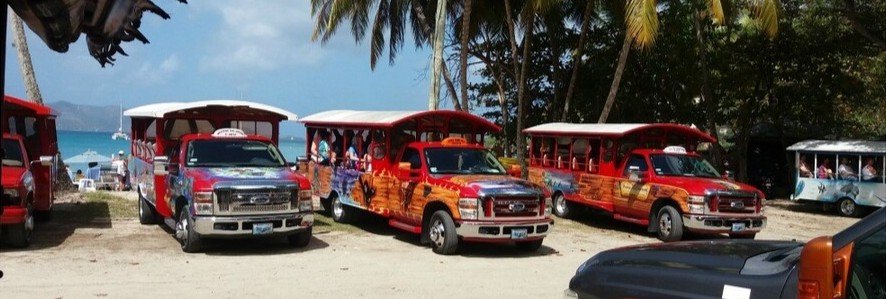 Colorful open-air safari taxis parked near a beach in Tortola