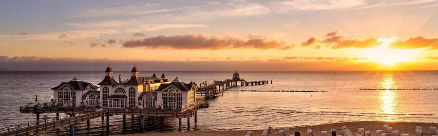 Sellin Pier at sunset on Rügen Island, Germany with golden sky, Baltic Sea horizon, and historic seaside pavilion.
