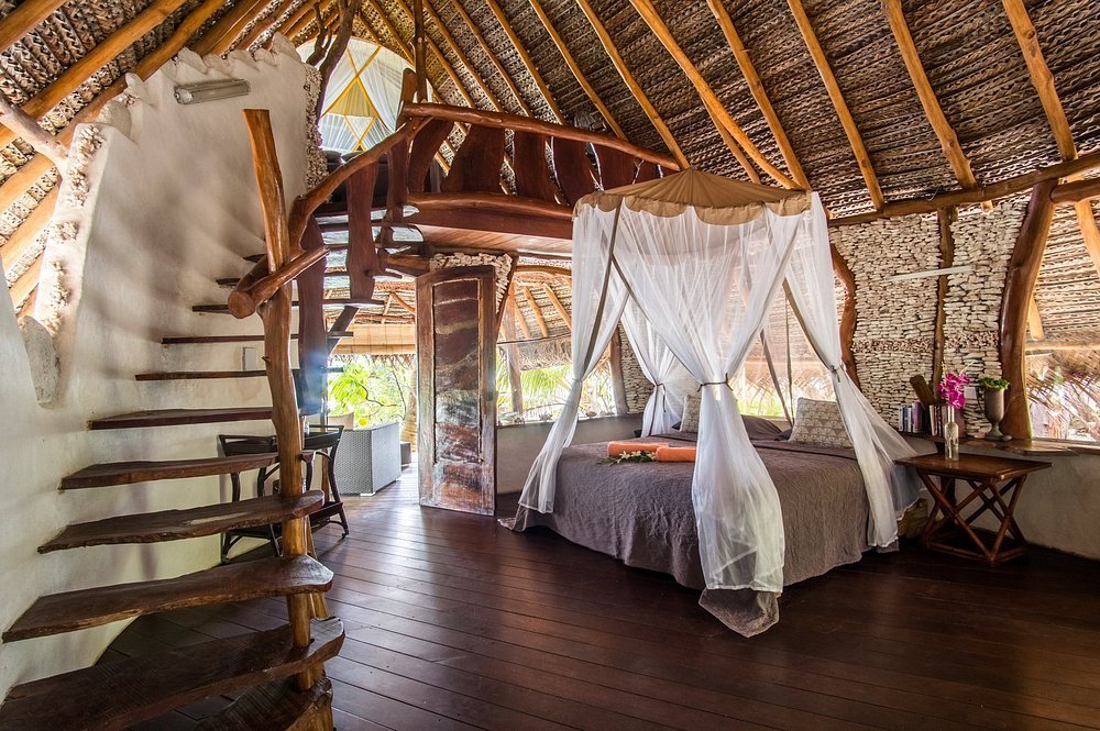 Ninamu Resort bedroom interior with canopy bed, wooden staircase, and open-air tropical design