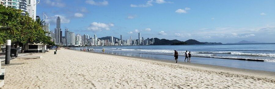 Avenida Atlantica along Copacabana Beach in Rio de Janeiro Brazil with sandy shoreline, ocean waves, and city skyline in the background.