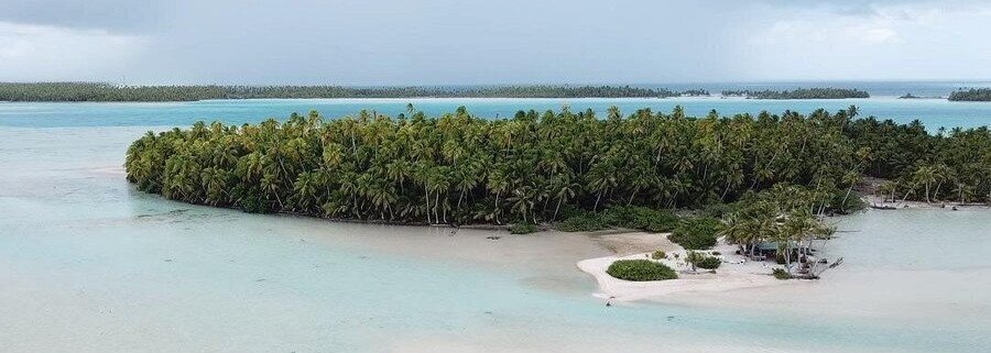 Private island in Rangiroa’s Blue Lagoon with palm trees, shallow turquoise water, and a small pink sand beach