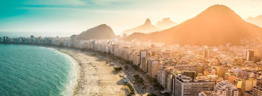 Aerial view of Copacabana Beach in Rio de Janeiro Brazil with the famous curved coastline, city skyline, and mountains glowing at sunset.