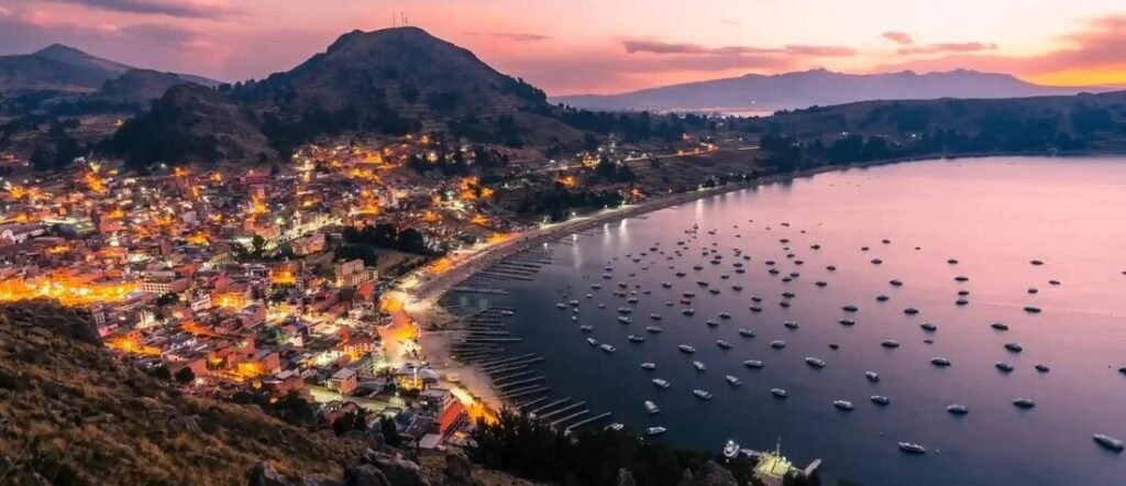 Sunset view of Copacabana Beach in Rio de Janeiro with glowing city lights and boats in the calm bay.