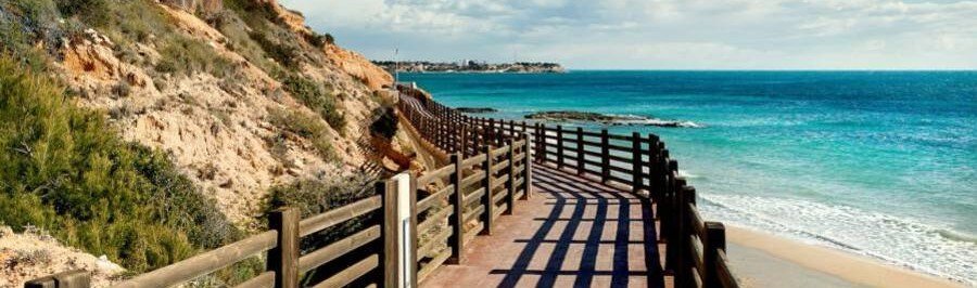Wooden coastal walkway along cliffs overlooking sandy beach and turquoise Mediterranean Sea on the Costa Blanca Spain